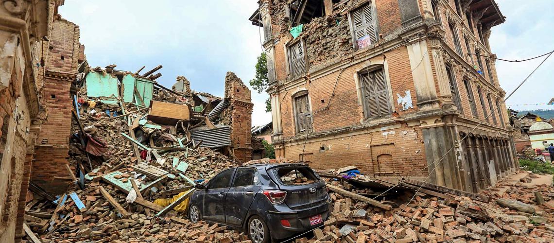 A destroyed car cloaked in debris from collapsed houses
