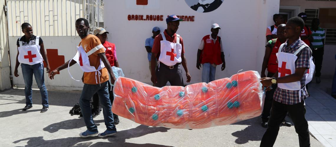 Two Red Cross Volunteers carrying water gallons outside a Red Cross Post