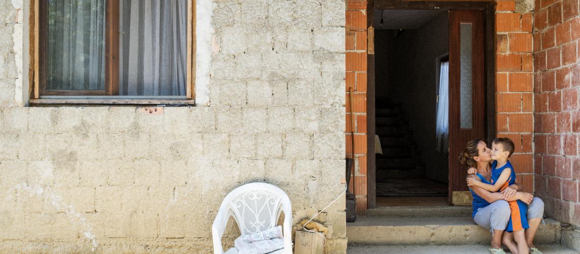 Woman and male child hugging in front of a house entrance