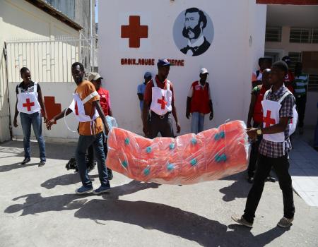 Two Red Cross Volunteers carrying water gallons outside a Red Cross Post