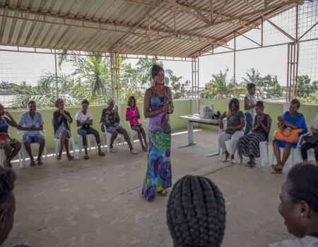 A woman standing in the middle of a goup of people sitting in a gathering